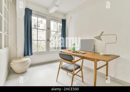 Modernes Interieur des geräumigen Zimmers mit Holztisch und Sessel in der Nähe des Fensters in hellen Wohnung eingerichtet Stockfoto