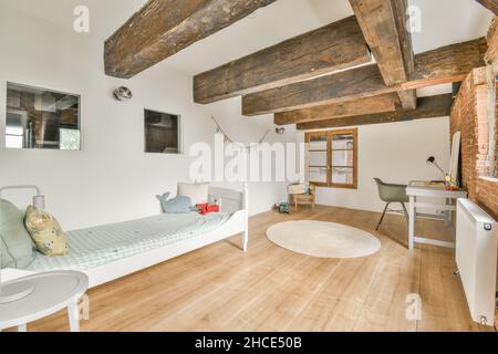 Stilvolles Interieur des geräumigen Schlafzimmers mit Backsteinwand mit Bett neben Tisch mit Sessel in moderner Wohnung eingerichtet Stockfoto