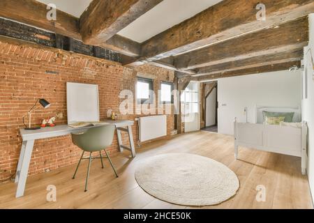 Stilvolles Interieur des geräumigen Schlafzimmers mit Backsteinwand mit Bett neben Tisch mit Sessel in moderner Wohnung eingerichtet Stockfoto
