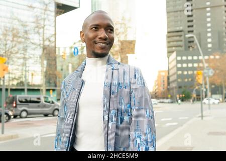 Inhalt kahlköpfiger afroamerikanischer Mann in modischer Kleidung, der mit einem Lächeln auf der Straße in der Stadt steht Stockfoto