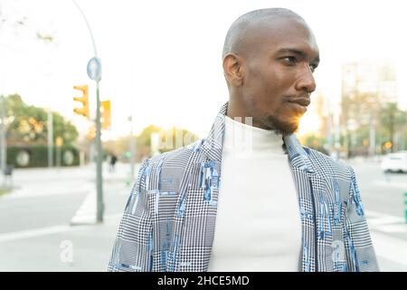 Kahlköpfiger afroamerikanischer Mann in modischer Kleidung, der auf der Straße in der Stadt wegschaut Stockfoto