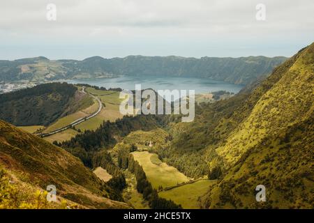 Spektakuläre Aussicht auf grünen Berghang mit Bäumen und See umgeben von felsigen Klippen auf den Azoren, Sao Miguel Stockfoto