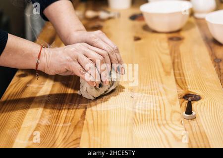 Crop unkenntlich weibliche Handwerker rollendes Stück Ton auf Holztisch mit Schüsseln in der Werkstatt Stockfoto