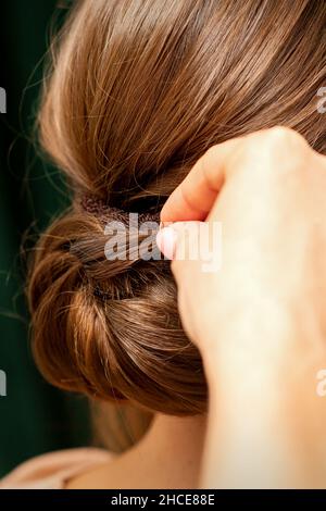 Friseurhands, die französische Frisur einer nicht erkennbaren jungen Brünette in einem Schönheitssalon drehen, Rückansicht, Nahaufnahme Stockfoto
