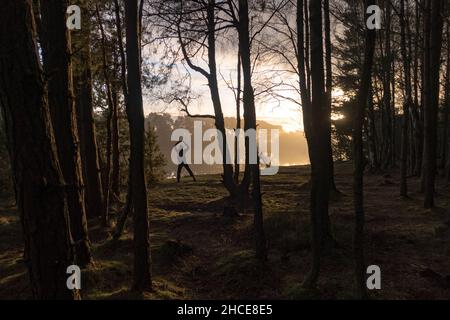 Eine Person, die im Winter in einem Wald am Fluss eines Sees bei Sonnenuntergang Übungen macht Stockfoto