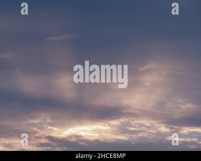 Wolkiger Himmel. Rote Strahlen der untergehenden Sonne durchdringen den Riss in den Wolken und erzeugen spektakuläre Streifen. Stockfoto