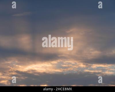 Wolkiger Himmel. Rote Strahlen der untergehenden Sonne durchdringen den Riss in den Wolken und erzeugen spektakuläre Streifen. Stockfoto