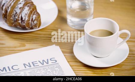 tasse Kaffee mit Milch in der Nähe von Zeitung, Glas Wasser und Croissant, Stockbild Stockfoto
