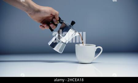 Teilansicht des Mannes, der Espresso in die Tasse gießt, auf weißem und grauem Bild Stockfoto