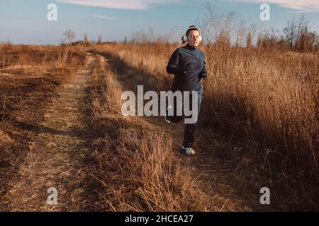 Sportliche junge Frau läuft im Park und hört Musik. Herbstwaldweg. Stockfoto