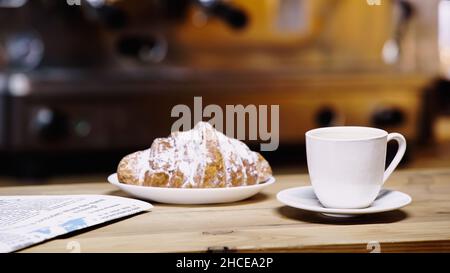 tasse Kaffee in der Nähe von Croissant auf dem Teller und Zeitung auf dem Tisch, Stockbild Stockfoto