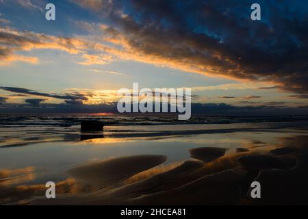 Wolkiger Morgenhimmel reflektiert auf Sand und Wasser bei Sonnenaufgang Stockfoto