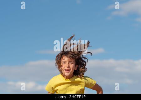 Junger hübscher Junge mit langen Haaren springt und lacht Blick auf die Kamera. Konzept Spaß und Freizeit Freizeit