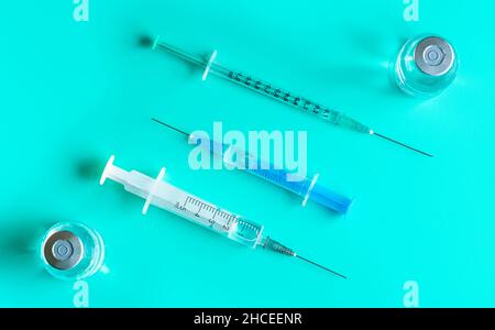 Hypodermische Spritzen und Nadeln mit Impfstoffflaschen auf dem Cyan-Tisch, Ansicht von oben Stockfoto