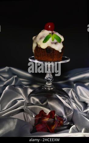 Festlicher Cupcake (Geburtstag, Valentinstag) mit Schlagsahne, Kirschen und Minze verziert Stockfoto