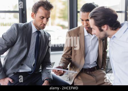 Multiethnische Geschäftsleute, die während der Diskussion im Büro auf ein digitales Tablet blicken Stockfoto