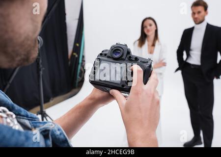 Professioneller Fotograf, der im Fotostudio den Sucher einer Digitalkamera in der Nähe von verschwommenen Modellen betrachtet Stockfoto