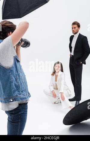 Junge Models in schwarz-weißen Anzügen posieren in der Nähe des Fotografen auf weiß Stockfoto