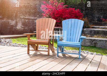 Leere farbenfrohe Adirondack-Stühle auf einer Promenade mit Blumen im Hintergrund an einem sonnigen Herbstmorgen Stockfoto