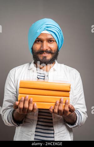 Porträtaufnahme eines jungen lächelnden sikh-Mannes, der mit Büchern auf die Kamera schaut - Konzept von Bildung, Wissen und Aspient. Stockfoto