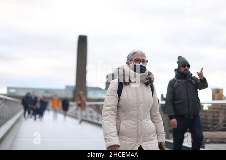 Die Menschen laufen in Gesichtsbezügen entlang der Millennium Bridge in London. Es wurde bekannt gegeben, dass in England vor dem neuen Jahr keine weiteren Beschränkungen für Coronaviren eingeführt werden. Bilddatum: Dienstag, 28. Dezember 2021. Stockfoto