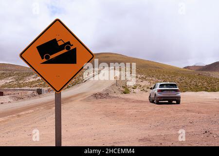 Warnschild am steilen Hang und ein Auto am Straßenrand Stockfoto