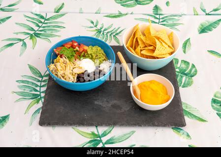 Ein komplettes mexikanisches Menü mit schwarzen Bohnen mit gezupftem Huhn, Queso Fresko, Avocado, gehackten Tomaten, geschmolzenem Cheddar-Käse und Maischips Stockfoto