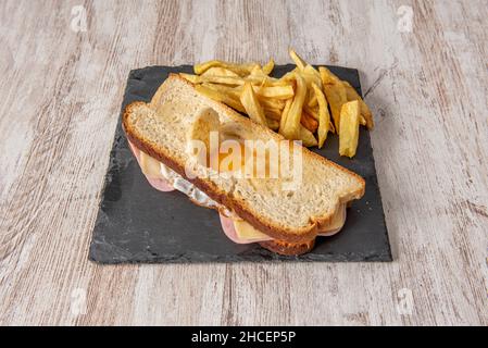 Kubanisches Sandwich mit Spiegelei, Käse und gekochtem Schinken, garniert mit hausgemachten Pommes auf einem Holztisch Stockfoto