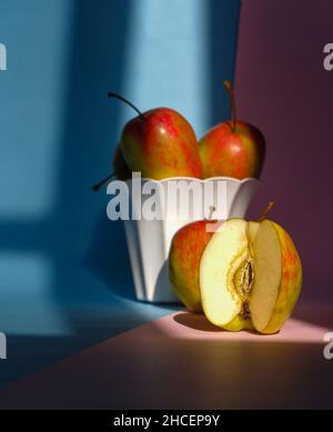 Foto eines Apfels in einem Behälter auf einem rosa und blauen Hintergrund Stockfoto