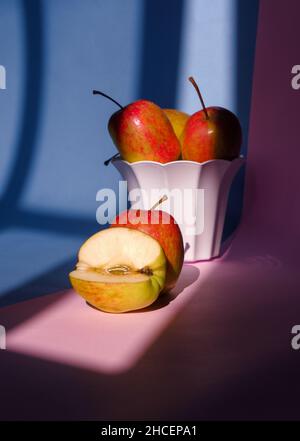 Foto eines Apfels in einem Behälter auf einem rosa und blauen Hintergrund Stockfoto