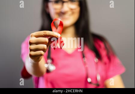 Der Arzt hält ein rotes Abzeichen in den Händen, um den AIDS Day zu unterstützen. Konzept für Gesundheit, Medizin und AIDS-Bewusstsein. Stockfoto