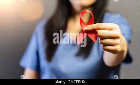 Der Arzt hält ein rotes Abzeichen in den Händen, um den AIDS Day zu unterstützen. Konzept für Gesundheit, Medizin und AIDS-Bewusstsein. Stockfoto