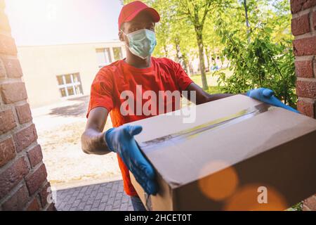 Delivery Mann Mitarbeiter in roten Kappe blank T-Shirt Uniform Gesichtsmaske Handschuhe halten leere Karton-Box. Service Quarantäne Pandemie Coronavirus Virus 2019 Stockfoto