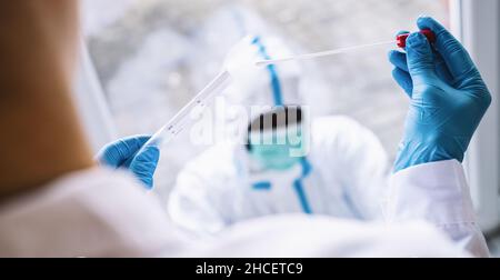 Medizinische Fachkraft in Schutzkleidung nimmt während der Coronavirus-Epidemie den COVID-19 Tupfer-Reagenzglaskasten im Covid-19-Testzentrum ein. PCR-DNA-Tests pro Stockfoto