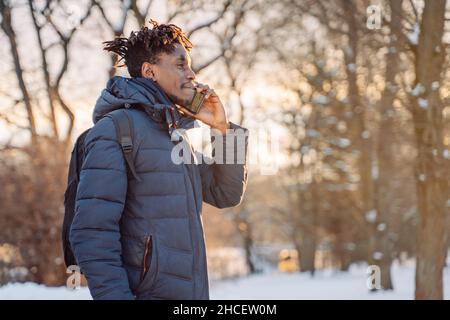 Ein junger afrikanischer Mann in Jacke und Rucksack telefoniert auf der Straße der Stadt. Tourismus, Urlaub in Europa, Kommunikation. Stockfoto