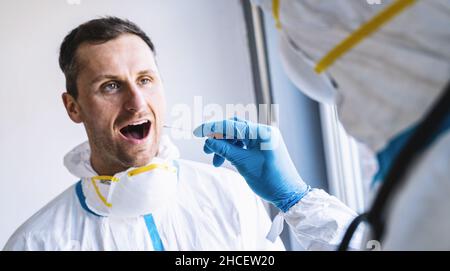 Ein Arzt in Schutzkleidung nimmt während einer Coronavirus-epid einen Tupfer aus dem Mund eines erschöpften Arztes in einem Covid-19-Testzentrum Stockfoto