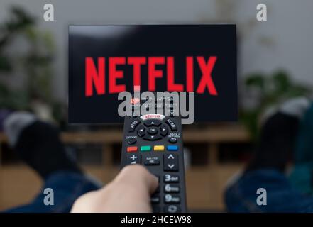 TV-Fernseher Netflix-Logo auf dem Bildschirm mit Fernbedienung zu Hause. Stockfoto