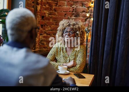 Afrikanische junge Geschäftsfrau im Gespräch mit einem Geschäftsmann während der Kaffeepause beim Treffen im Café Stockfoto