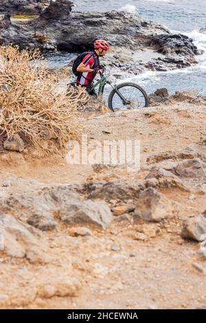 Mountainbiker schiebt sein E-Bike auf rauem Untergrund an der Küste in der Nähe von Los Abrigos, Teneriffa, Kanarische Inseln, Spanien, einen steilen Hang hinauf Stockfoto