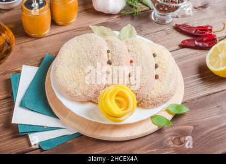 Frische Koteletts, Halbfertigprodukte für Burger aus Geflügelfleisch auf einem weißen Teller auf dunklem Holzboden. Stockfoto