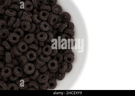 Haufen schwarzer Getreideringe isoliert auf weißem Hintergrund, leckere und nützliche Ringe Frühstückszerealien in einer Schüssel, Draufsicht aus der Nähe Stockfoto
