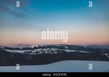 Eine orangefarbene Szene des schneebedeckten Berges und der Bäume im Nationalpark Niedere Tatra in der Slowakei bei Sonnenuntergang Stockfoto