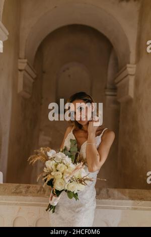 Schöne Braut aus dem Nahen Osten in ihrem weißen Brautkleid, das mit einem Blumenstrauß posiert Stockfoto