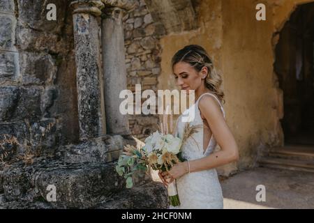 Schöne Braut aus dem Nahen Osten in ihrem weißen Brautkleid, das mit einem Blumenstrauß posiert Stockfoto