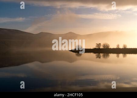 Hügel und Wolken spiegeln sich an einem Wintertag im Wasser des Stausees Stockfoto