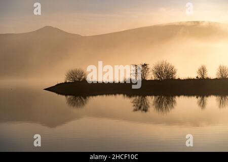 Hügel und Wolken spiegeln sich an einem Wintertag im Wasser des Stausees Stockfoto