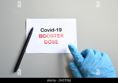 Die Hand des Arztes mit dem blauen Handschuh schreibt auf weißem Papier den Text „Covid-19 Booster Dose“. Konzept der Bekämpfung des COVID-19-Virus mit Third Stockfoto