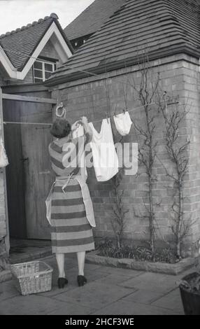 1950s, historisch, eine Dame, die vor einem Haus auf einer Terrasse stand und zum Trocknen einige gewaschene Kleidung an einer Wäscheleine aufhängte, England, Großbritannien. In diesem Jahrzehnt waren Wäscheleinen oder Wäscheleinen der natürliche Weg, Wäsche zu trocknen. Stockfoto