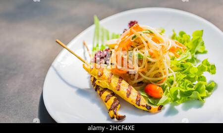Berühmter Thai Papaya Salat oder Sompum mit Hühnersatay auf der Seite Stockfoto