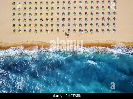 Blick von oben auf den Strand mit Strohschirmen. Regenschirme, Sand- und Meereswellen-Landschaft. Stockfoto